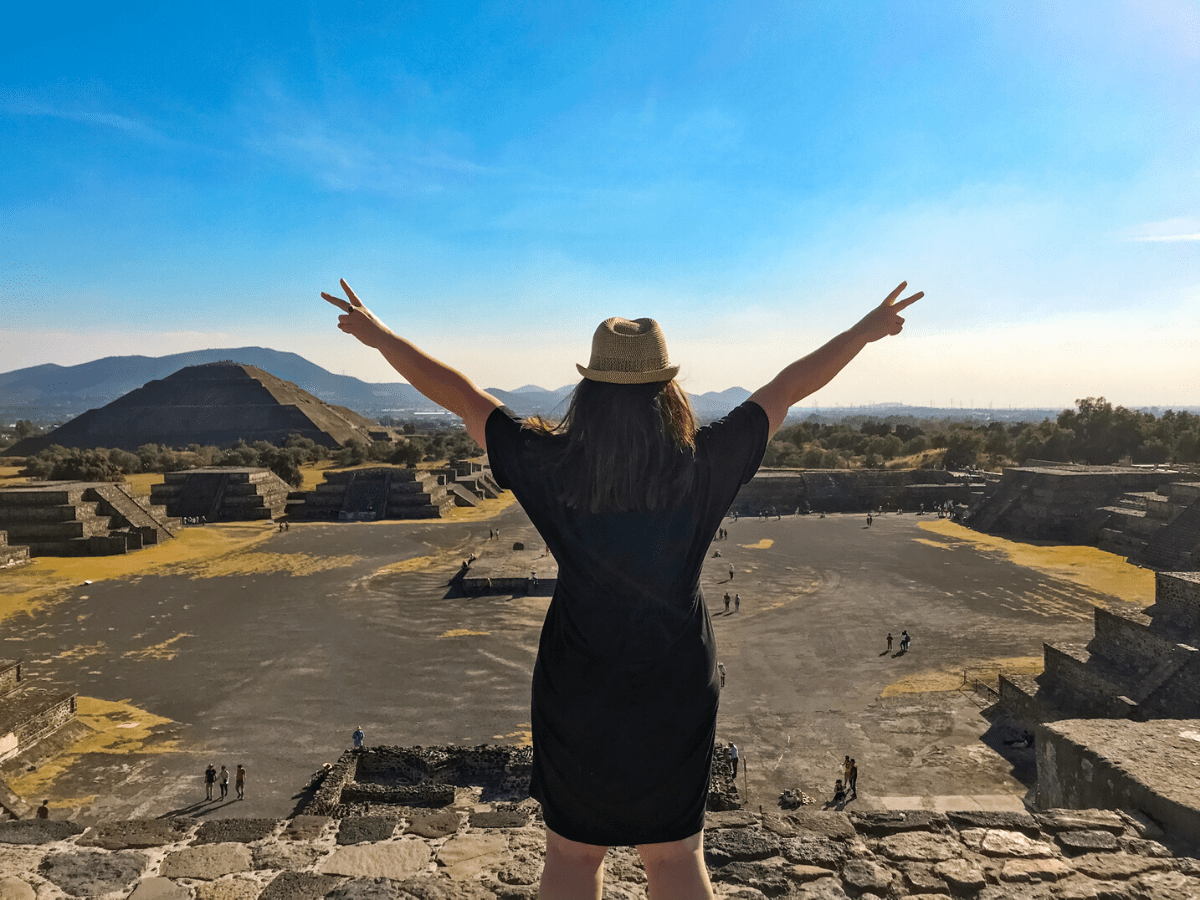 Woman solo traveler posing with both arms raised at the Temple of the Moon in Teotihuacan, Mexico