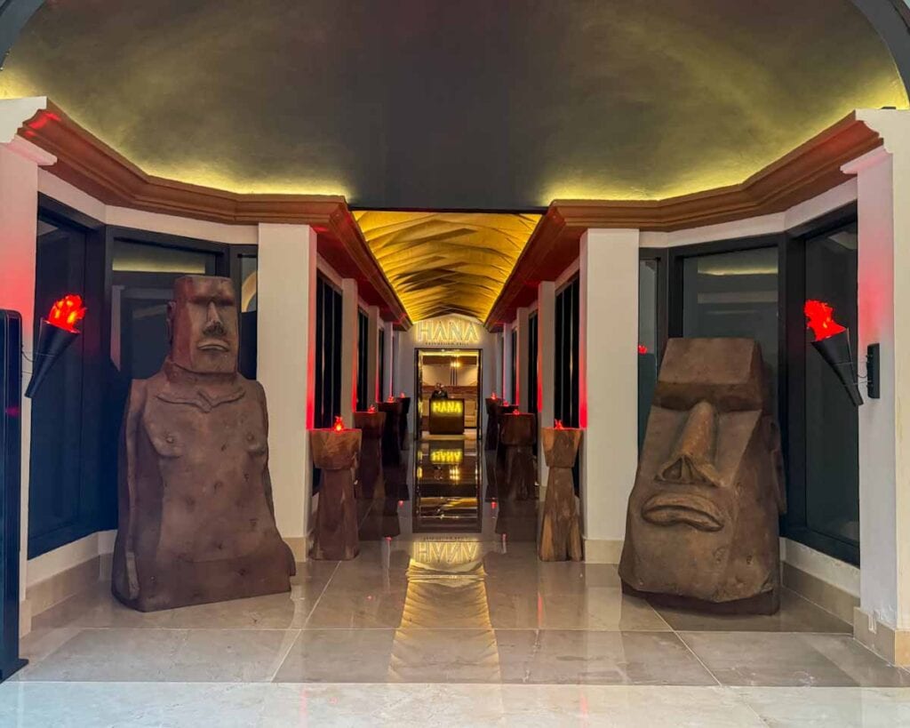 Hana Polynesian Grill entrance with large statues of heads and tiki torches